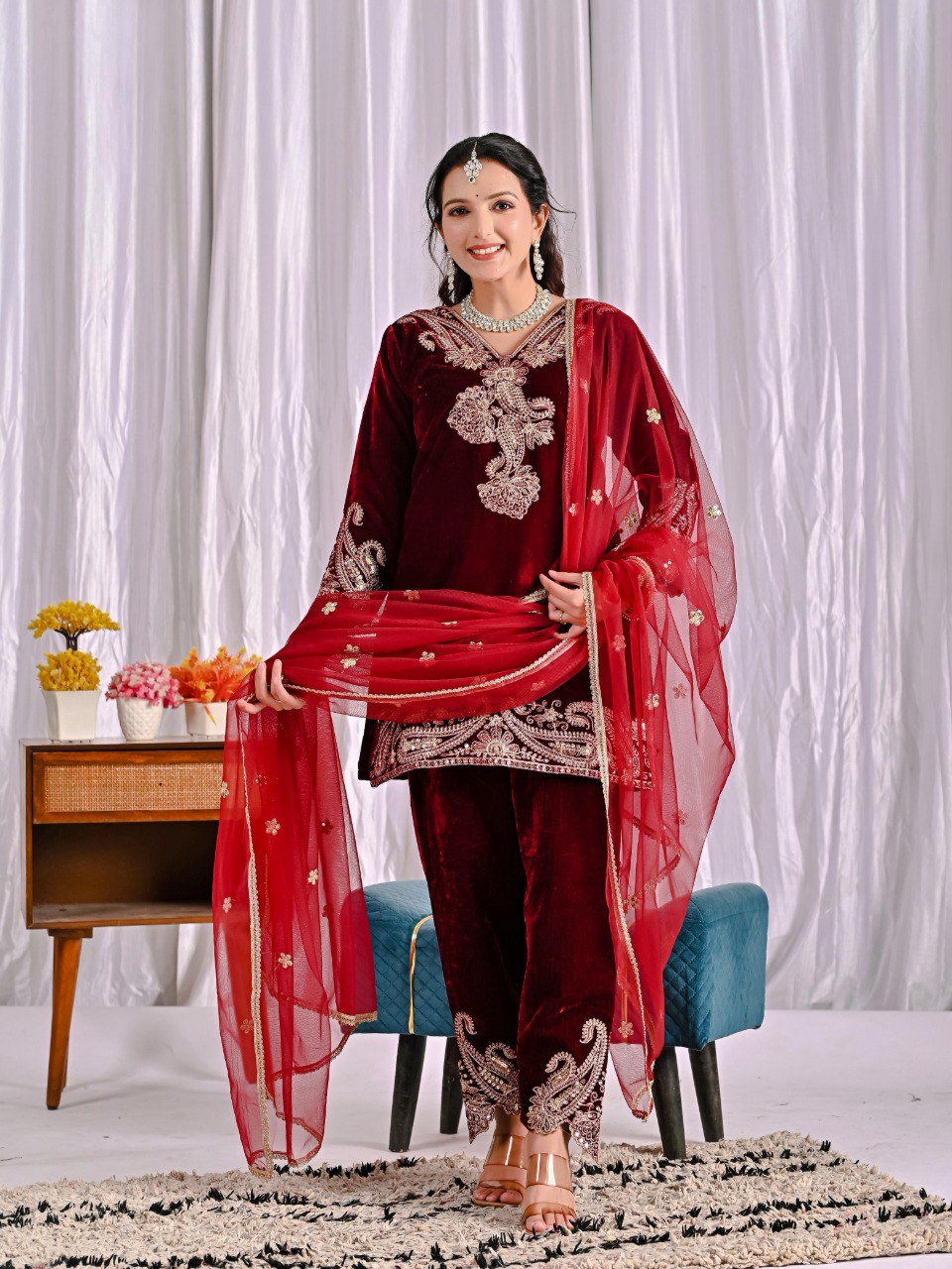 Model showcasing maroon velvet embroidered pant suit with net dupatta, smiling elegantly.