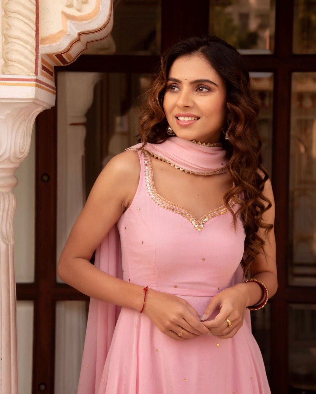 Woman smiling while wearing a pink georgette gown with sequence work and dupatta.