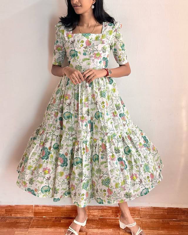 Woman posing in a white floral print tiered gown with square neck and short sleeves.