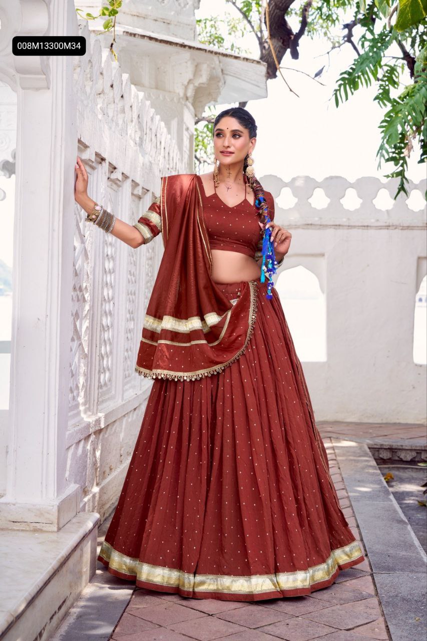 Model in TRENDBUY Reddish Orange Chanderi Lehenga Choli with Zari weaving and embossed lace border, standing elegantly in an outdoor setting.