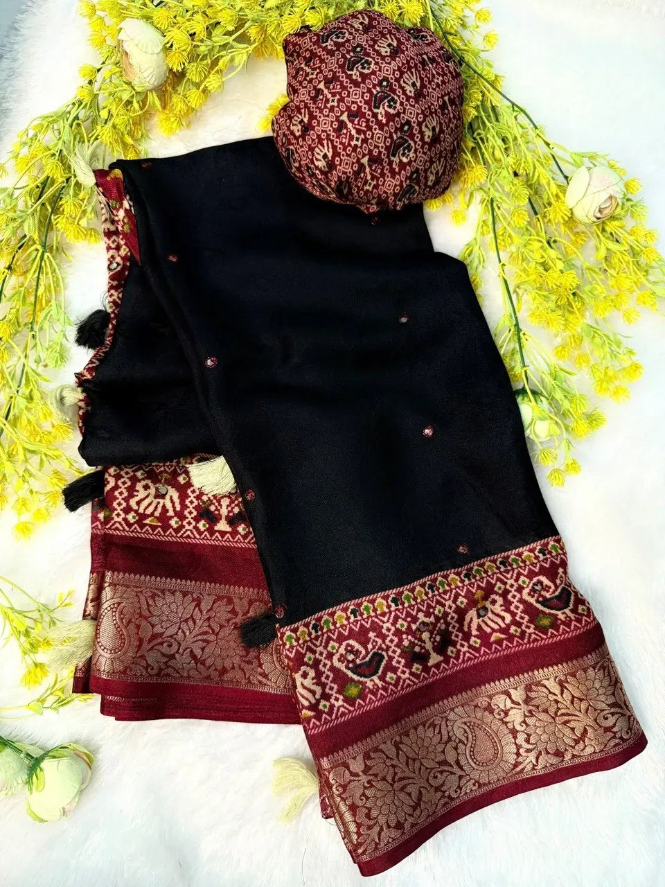 Black crepe silk saree with red and gold jacquard borders decorated with tassels and yellow flowers