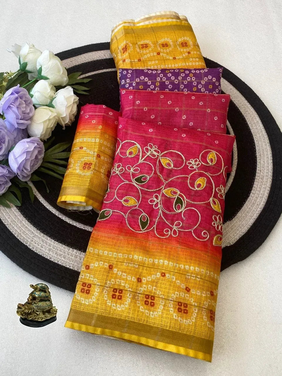 Folded multi-color Kota silk sarees with floral decor on round mat