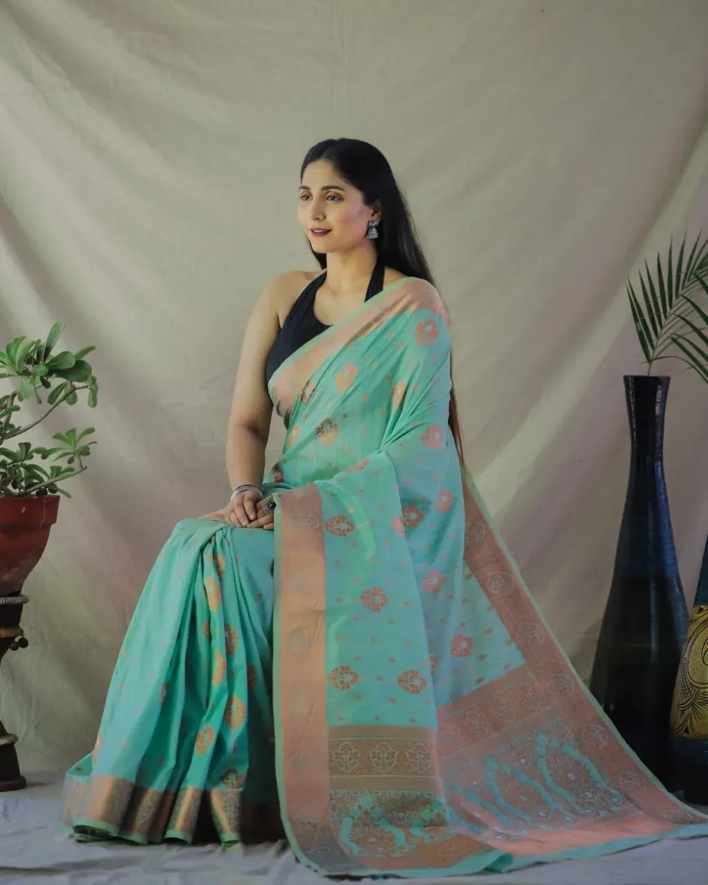 Model sitting gracefully wearing mint green jacquard silk saree with copper border