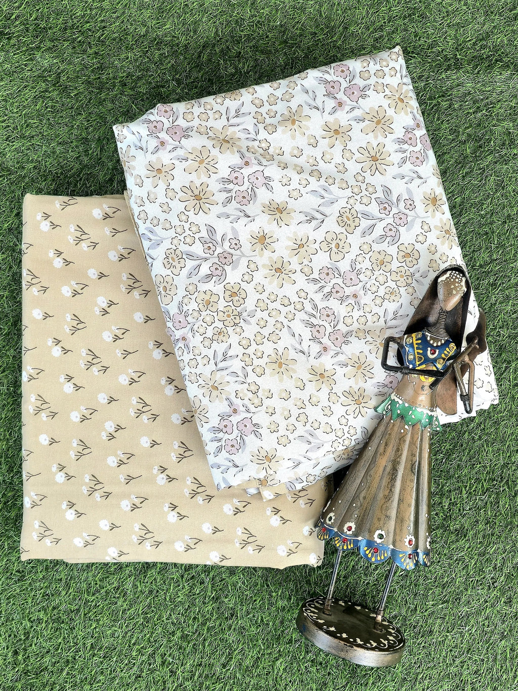 Cream and beige floral printed cotton single dohar folded on grass with decorative figurine