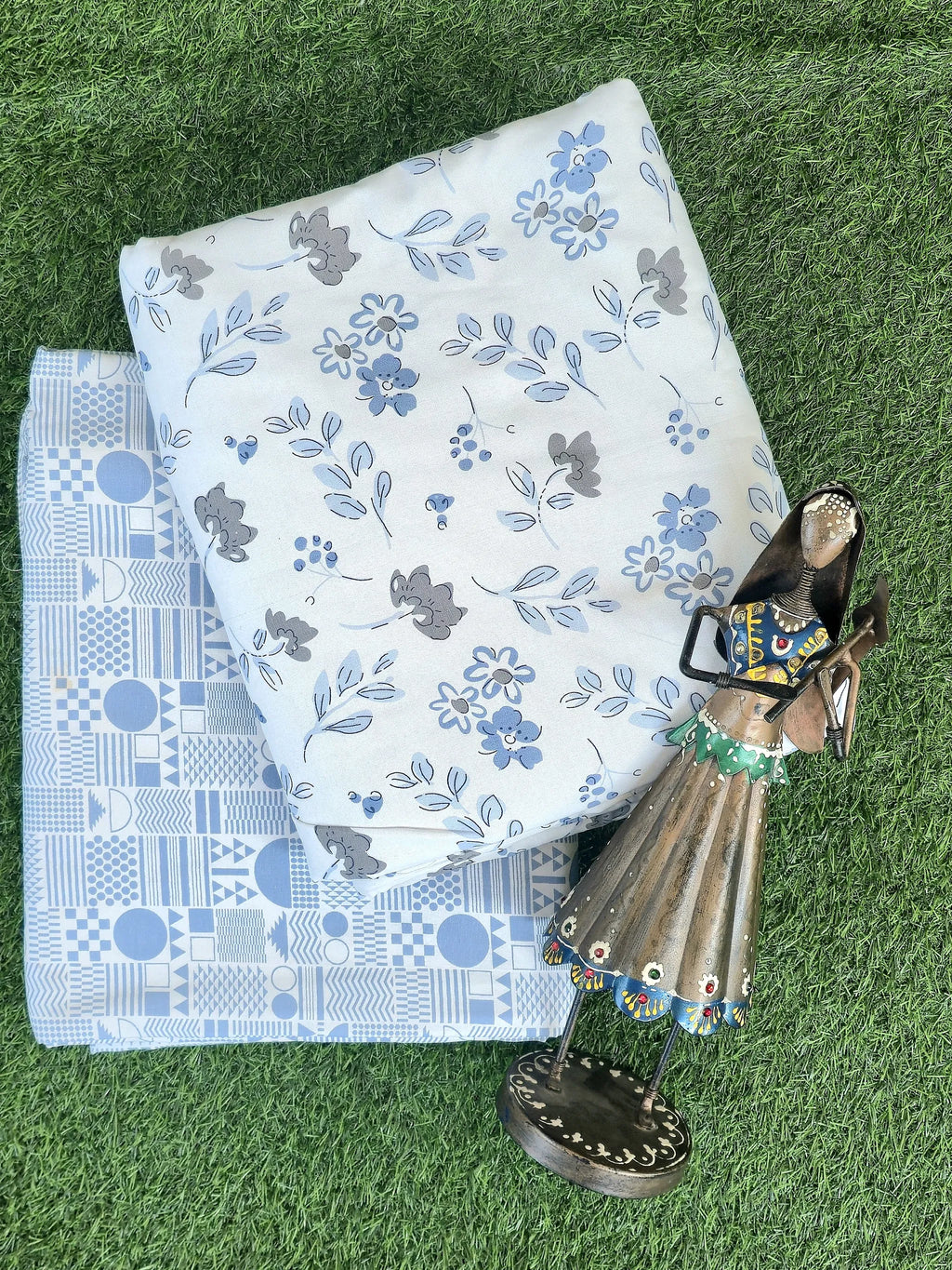 Light blue geometric and floral print cotton dohar folded on grass with decorative figurine
