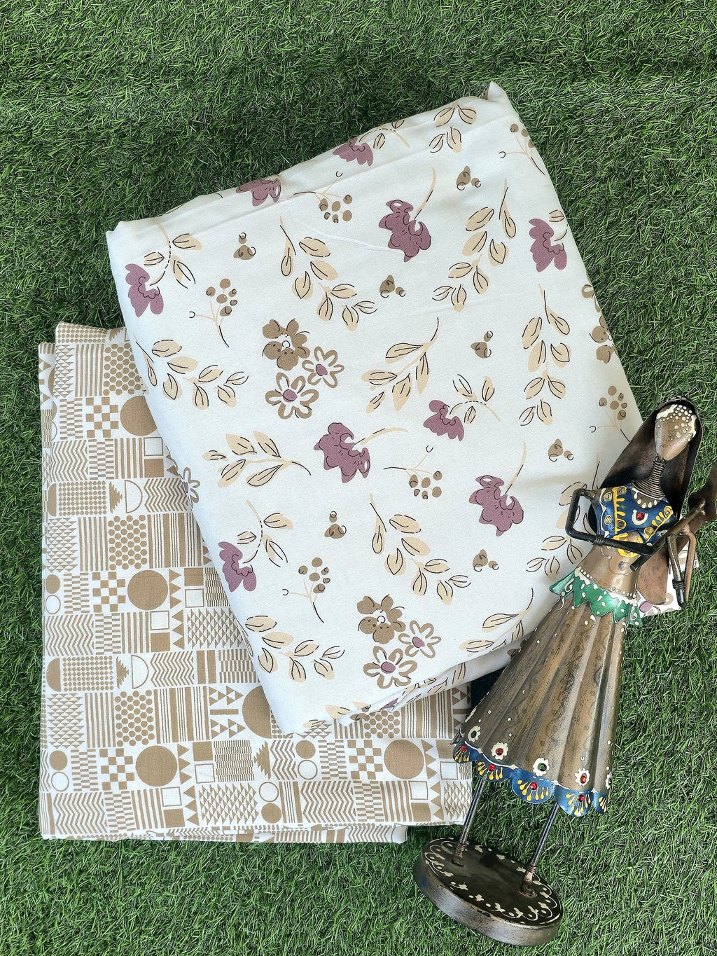 Folded white cotton dohar with purple floral print and beige geometric dohar on grass