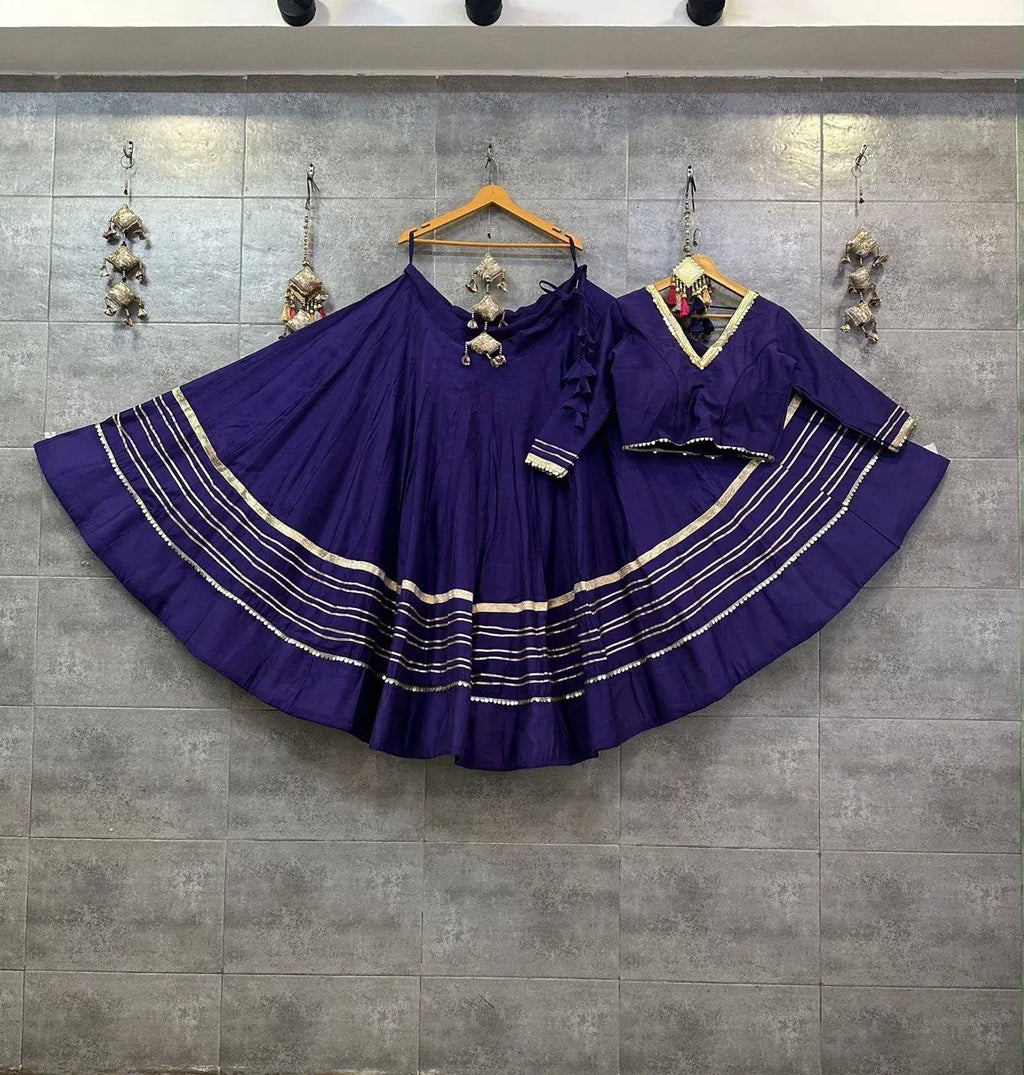 Deep purple rayon cotton chaniya choli with gold gota patti stripes hanging on a grey tiled wall