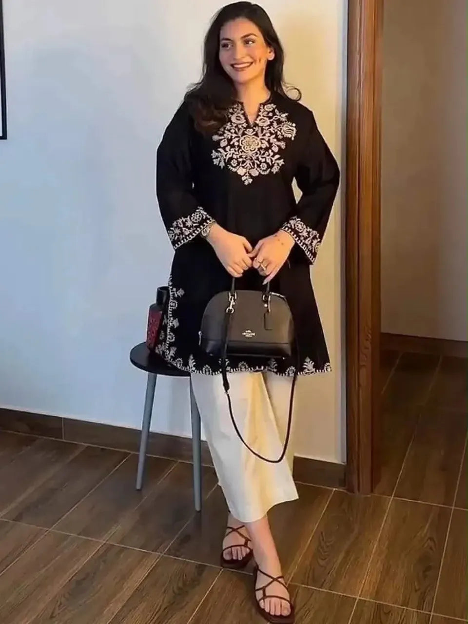 Model wearing black rayon cotton kurti with heavy chikankari embroidery and white pants holding a black bag