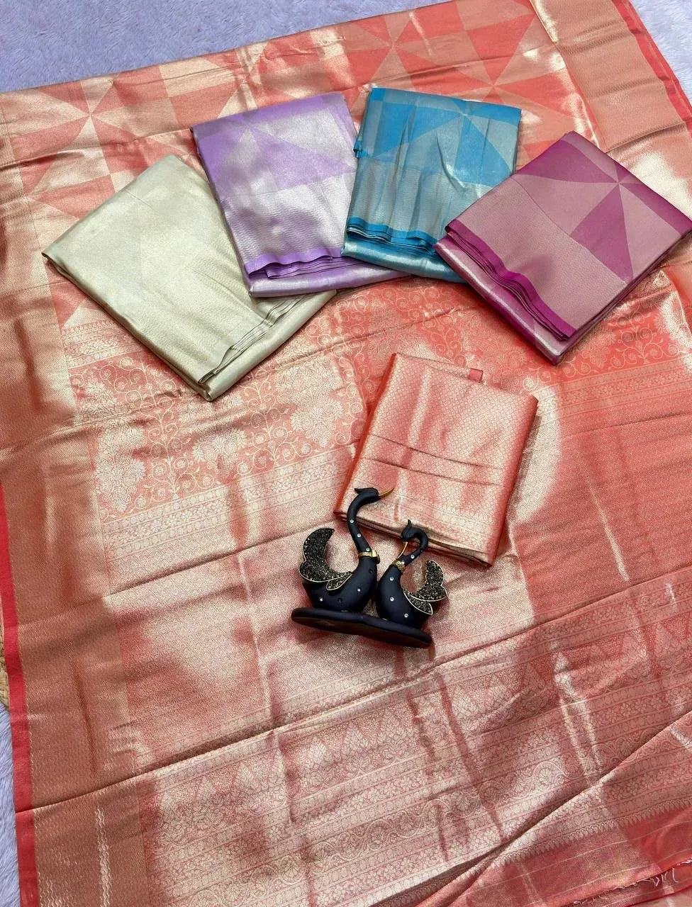 Flat lay of soft tissue satin silk sarees in multiple colors with swan showpiece