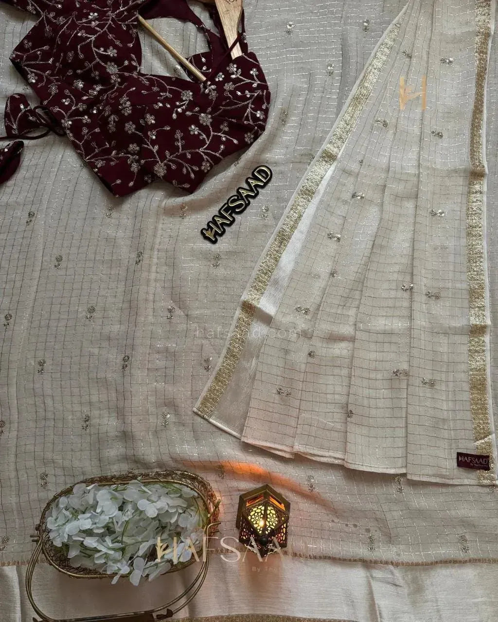 Flat lay of white georgette sequence saree with maroon embroidered blouse