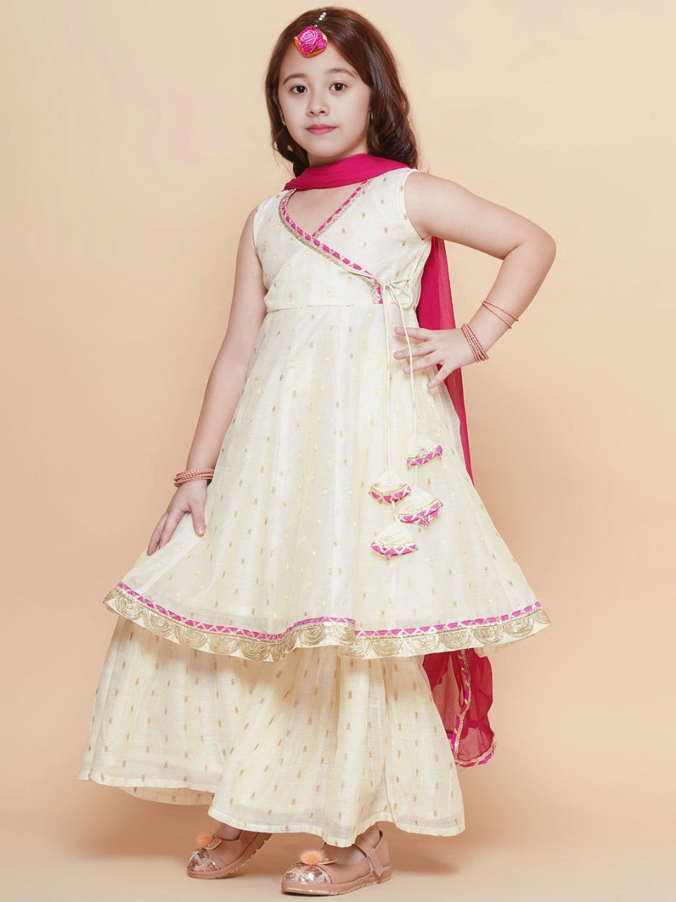 Young girl wearing a beautiful cream and pink printed Chanderi silk anarkali style sharara set with a fuchsia dupatta for a festive look.