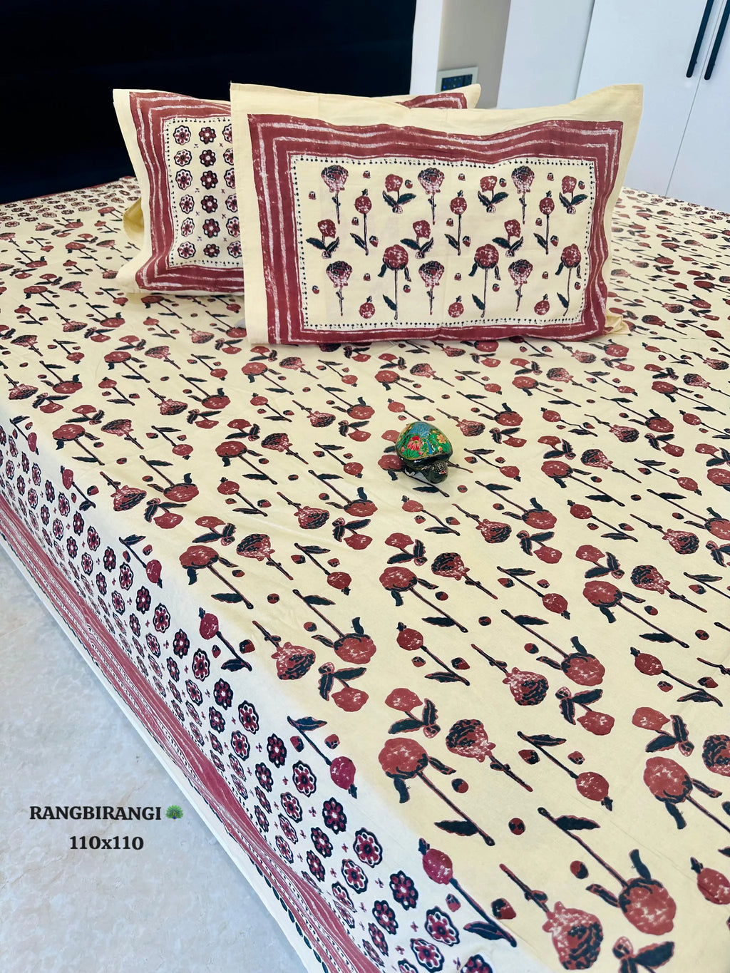 Cream and red floral block print cotton bedsheet with two matching pillow covers on bed
