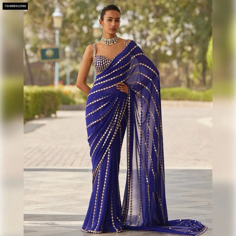 Model showcasing a royal blue pure georgette saree with intricate mirror and embroidery work, standing front-on outdoors.