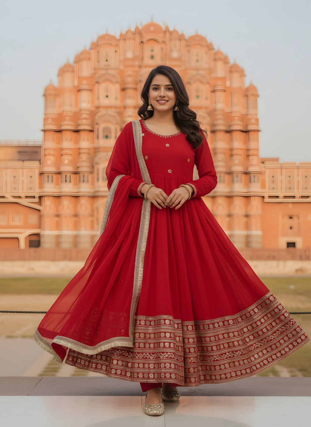 Full body shot of model wearing red Anarkali gown with intricate embroidery, posing gracefully in front of Hawa Mahal.