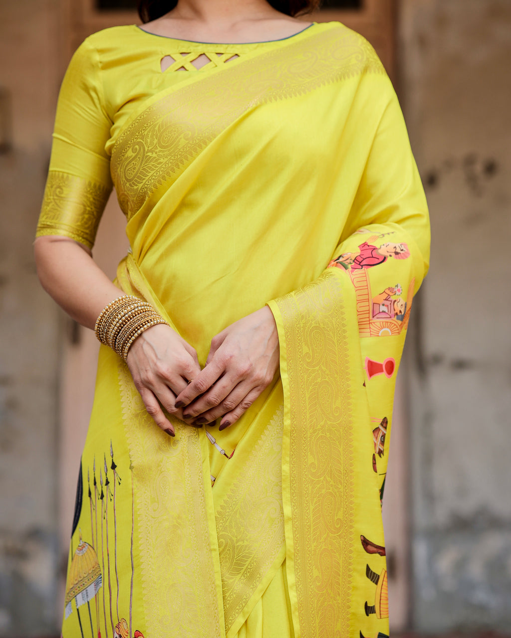 Close-up of a woman's midsection and hands, showing the rich Zari border and the exquisite heritage digital print on a yellow silk saree, with bangles.