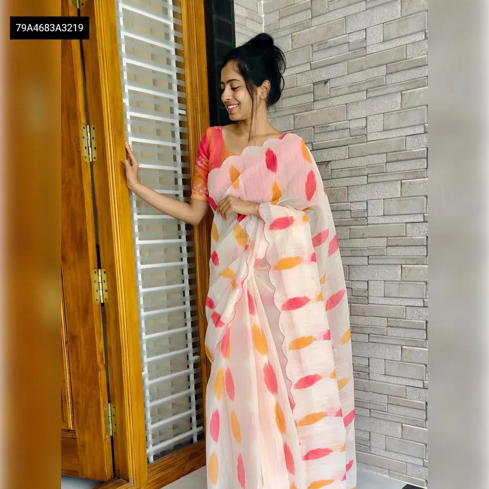 A smiling model gracefully posing in the white soft linen saree featuring vibrant multi-colored abstract prints, paired with the matching peach blouse, standing by a wooden door.