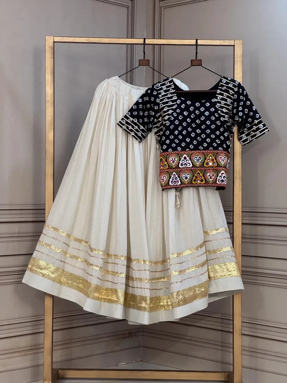 Off white cotton lehenga with gold borders paired with a black bandhej print blouse on a display stand