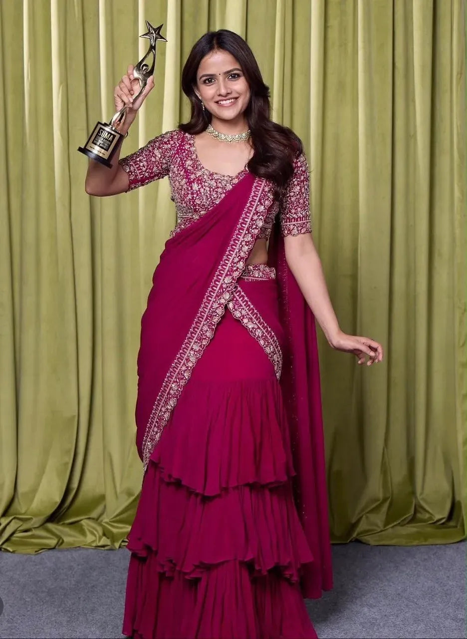 Model wearing maroon ruffle lehenga saree with heavy embroidery and holding trophy