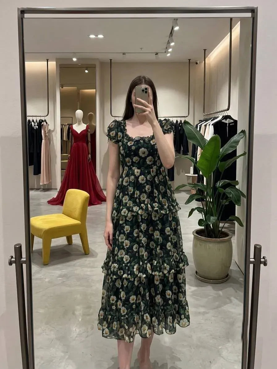 Woman wearing dark green floral maxi dress taking mirror selfie in boutique