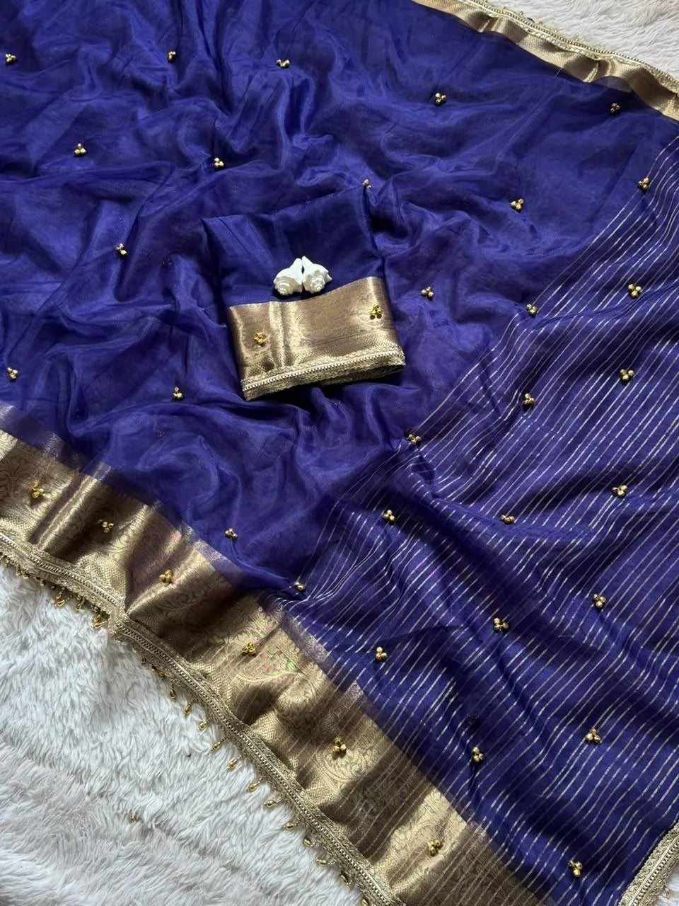 Royal blue soft tissue silk saree featuring gold border and delicate gold bead detailing on a white rug