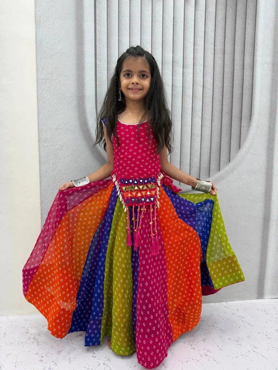 Young girl smiling in a vibrant multi-colored georgette lehenga choli with traditional bandhani print