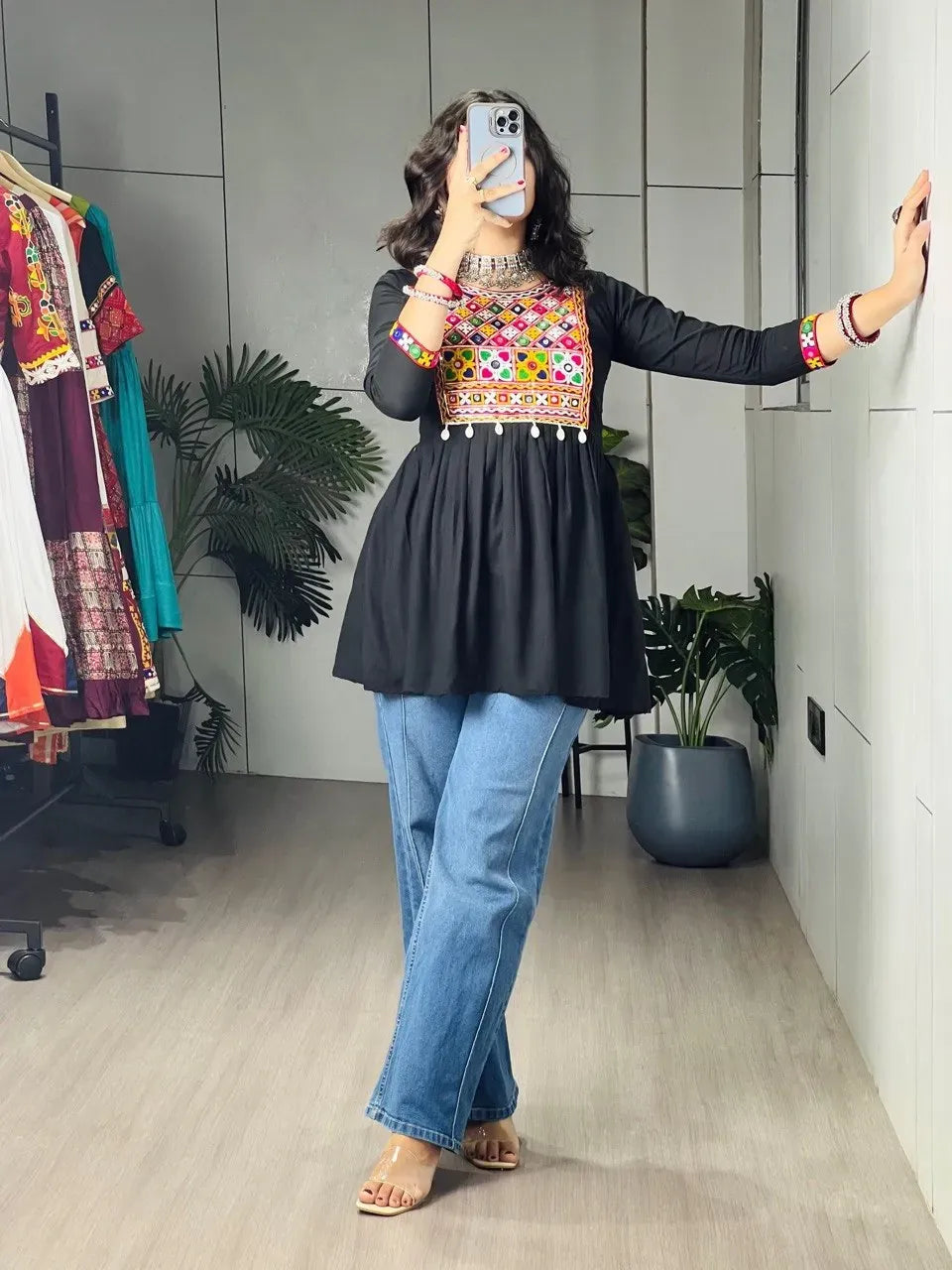Woman wearing a black Kediya top with vibrant Kutchi embroidery and mirror work paired with blue jeans