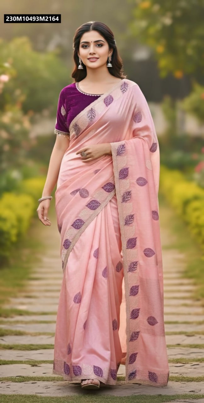 Model presenting a peach pink faux silk saree with stunning purple leaf embroidery and a rich royal purple blouse, in a vibrant garden environment.