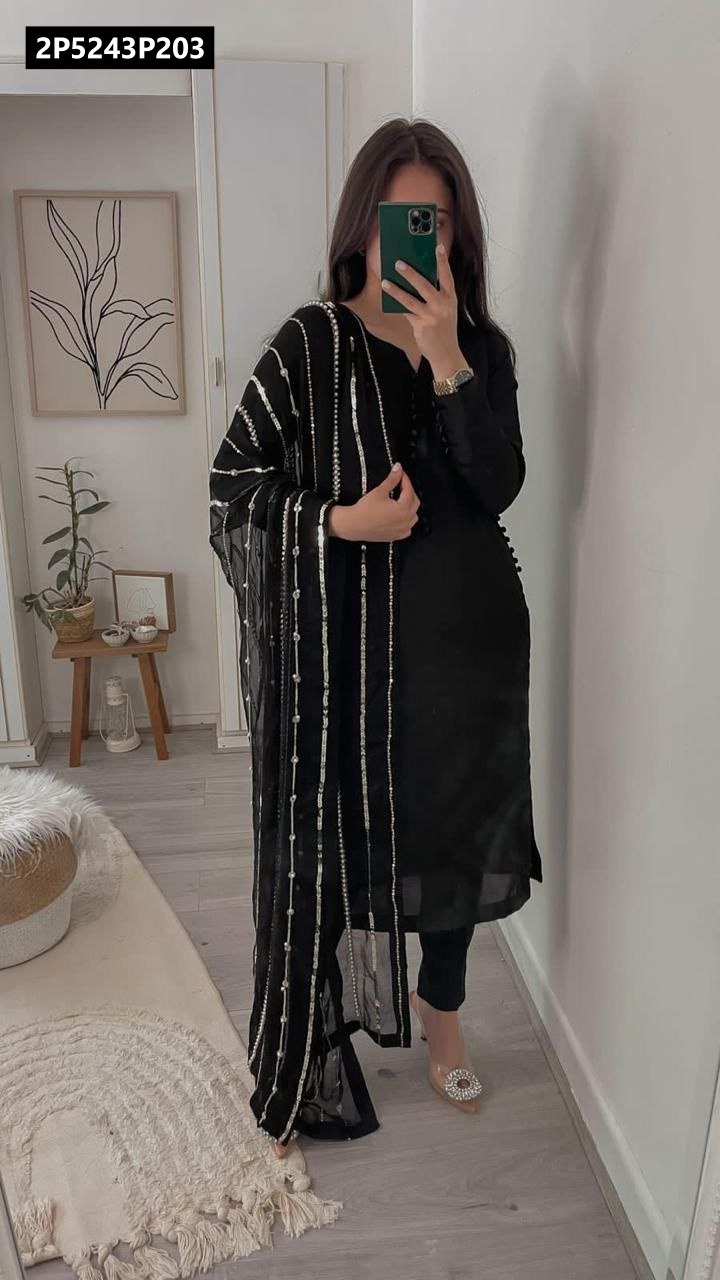 Full-length view of a woman wearing a black faux georgette kurta set with a heavily embroidered sequence dupatta, posing indoors.