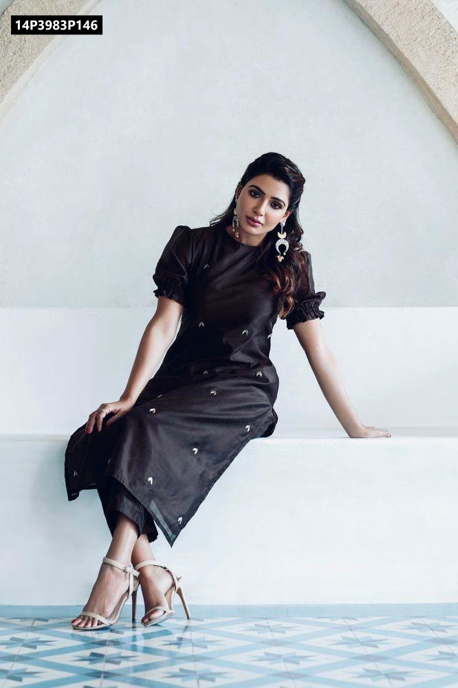Full body shot of a model sitting, wearing a black embroidered kurti with puff sleeves and matching pants, paired with nude heels.