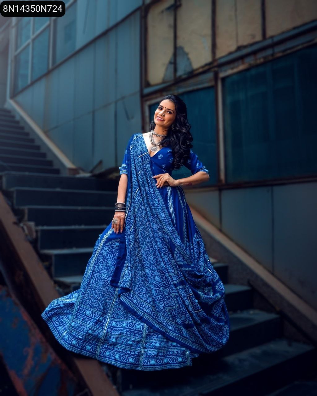 Stunning TRENDBUY model smiling in a blue Bandhani print Vaishali silk lehenga choli with Gota Patti, posing dynamically on industrial stairs.