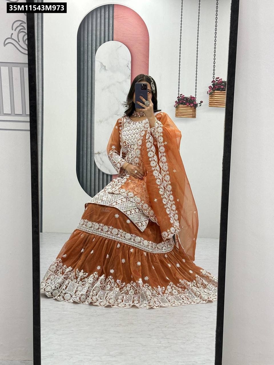 Model in TRENDBUY Burnt Orange Lily Net Farshi Sharara Suit, mirror selfie, seated pose, showcasing intricate white embroidery.