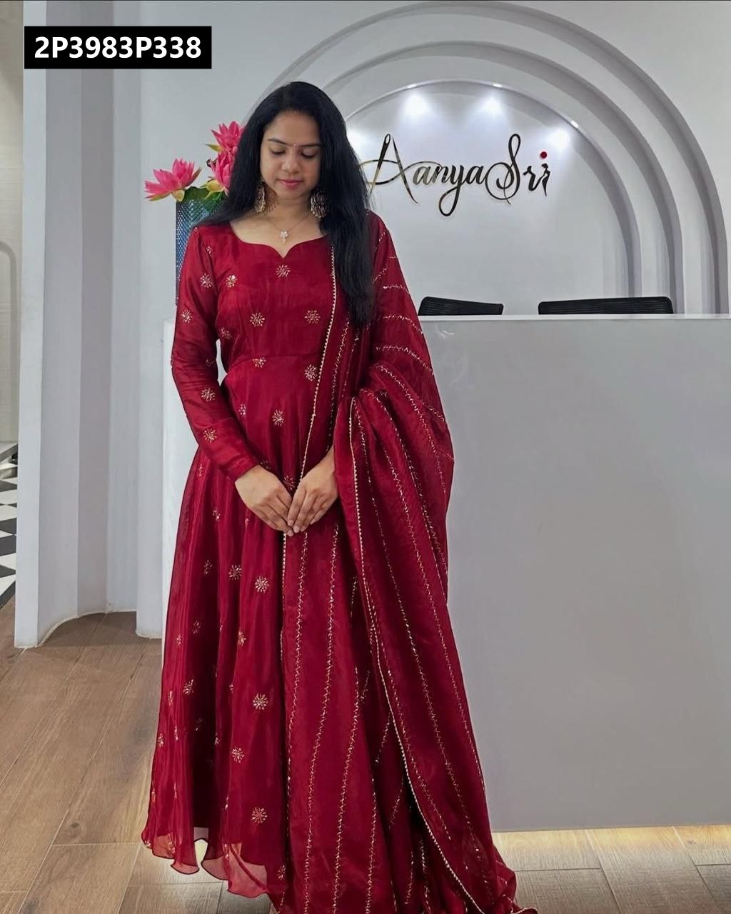 Elegant model wearing a full-length TRENDBUY Maroon Chinon Anarkali kurti with intricate golden embroidery, paired with a flowing matching dupatta, standing gracefully against a modern white reception background.