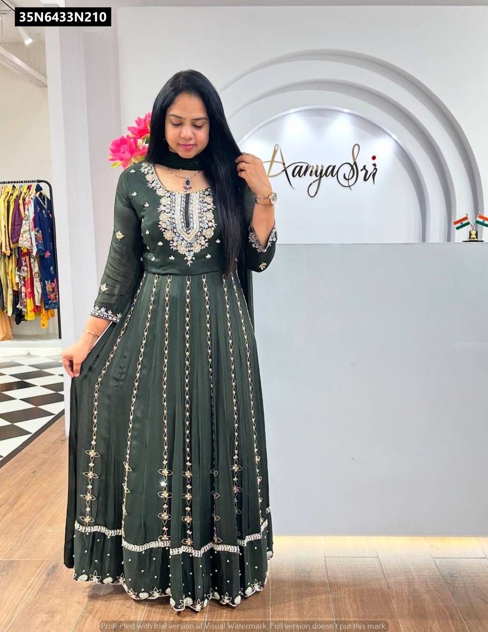 Full body shot of a model wearing an elegant dark green embroidered Chinon gown with a matching dupatta, standing in a chic boutique setting.