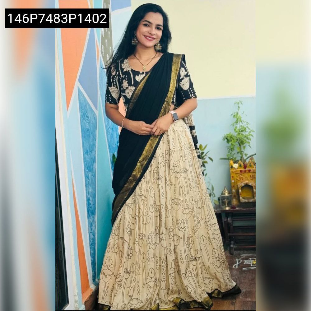 Full shot of a woman in a TRENDBUY Cream and Black Digital Printed Musline Silk Lehenga Choli set, smiling indoors against a colorful wall.