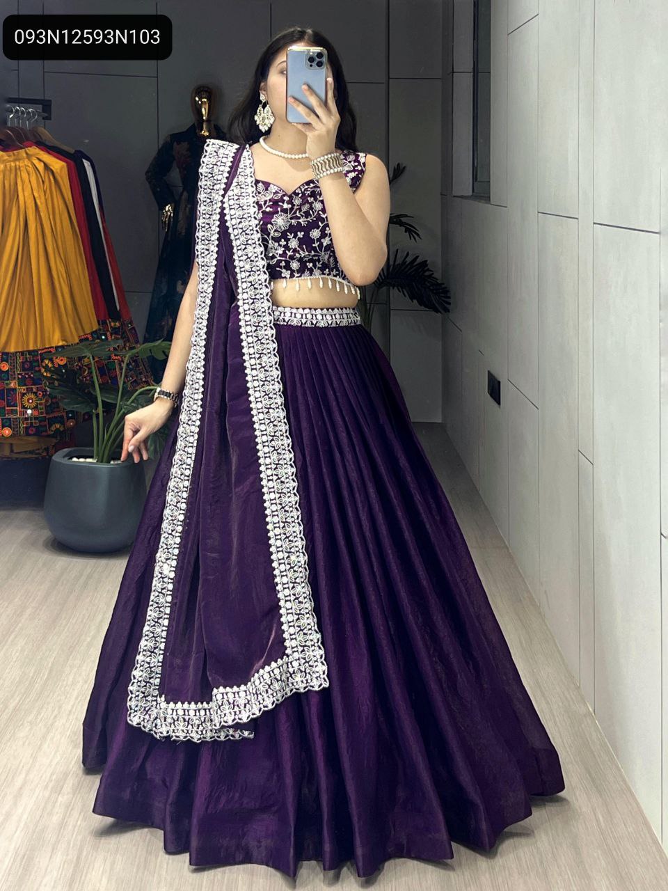 Model posing frontally, holding phone, showcasing the full Deep Purple Fendy Satin Silk Lehenga Choli with embroidered blouse and lace-bordered dupatta in an indoor setting.