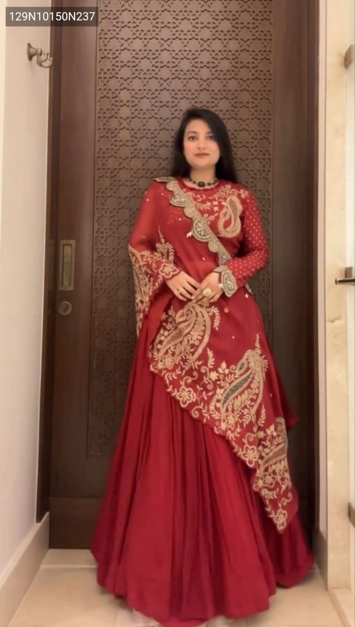 Model showcasing the TRENDBUY Designer Red Georgette Lehenga Choli set with gold cording sequence embroidery and a flowing shrug, standing against a patterned wooden door.