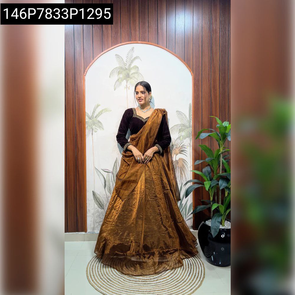 Full body shot of model elegantly posing in TRENDBUY deep brown velvet blouse and shimmering golden-bronze twill net lehenga set against a decorative wall.