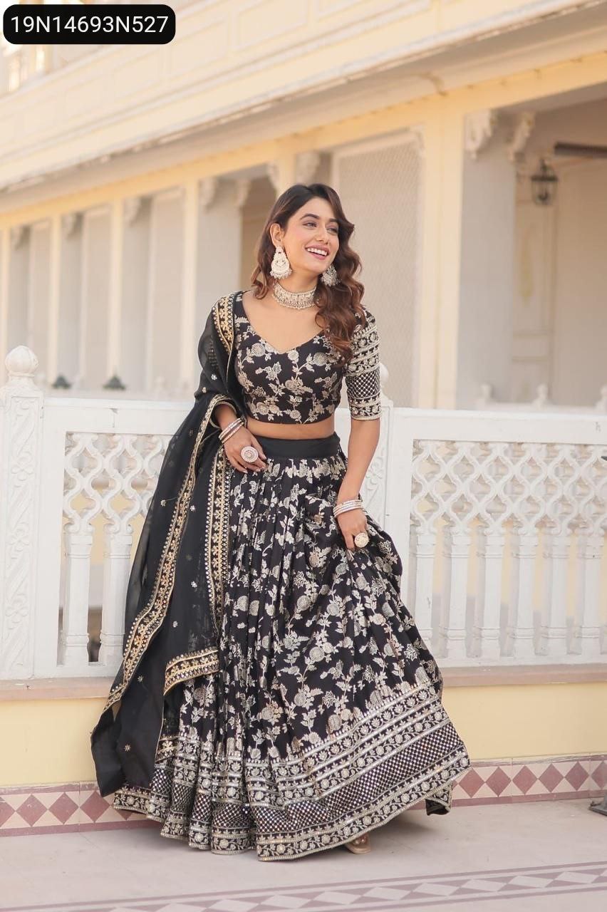 Smiling model in a Black TRENDBUY Viscose Jacquard Lehenga Choli with silver floral embroidery, posing against a white railing.