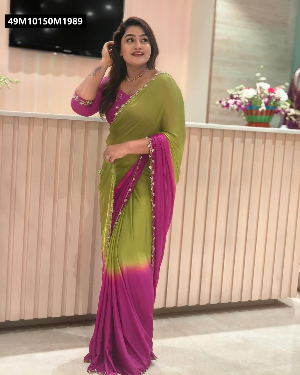 Woman smiling brightly while posing in an TRENDBUY olive green and fuchsia ombre chinnon saree with a matching blouse, standing against a light-colored wall.