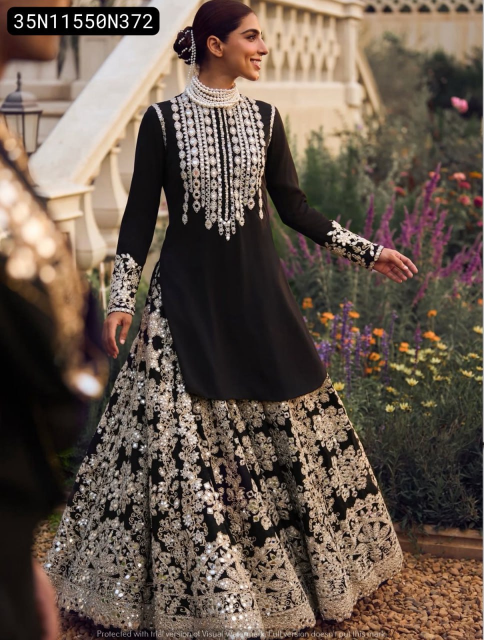 Elegant woman smiling, wearing a TRENDBUY black Chinon Lehenga Choli with heavy silver 7mm sequence embroidery, walking gracefully in a beautiful garden setting.