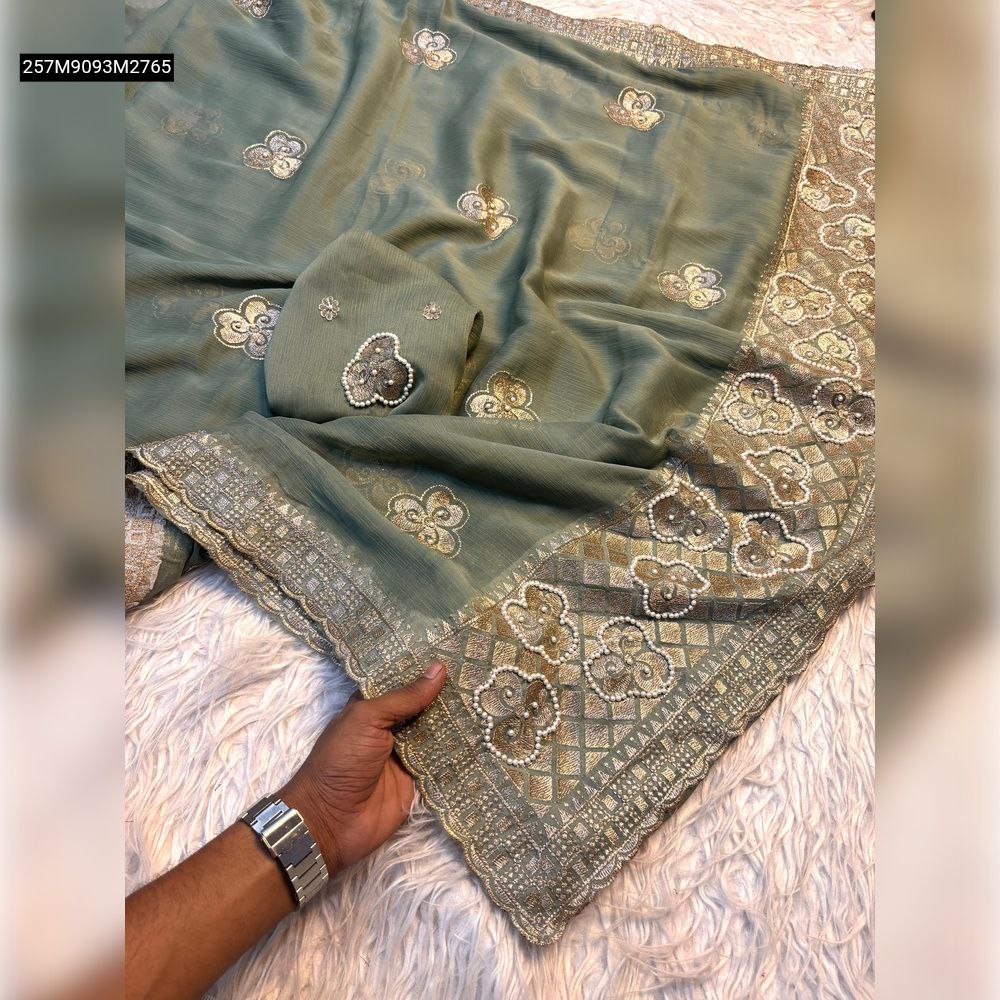 TRENDBUY Sage Green Chiffon Saree pallu with intricate golden zari and pearl floral embroidery, held by a hand on a white plush surface.