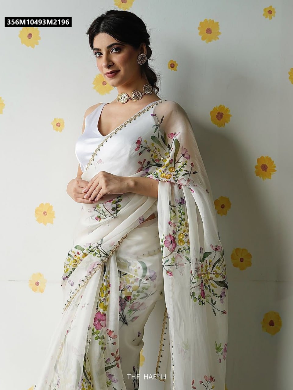 Close-up of a model's upper body wearing a white organza saree and a sleeveless white blouse, highlighting the floral design and sparkling jewelry.
