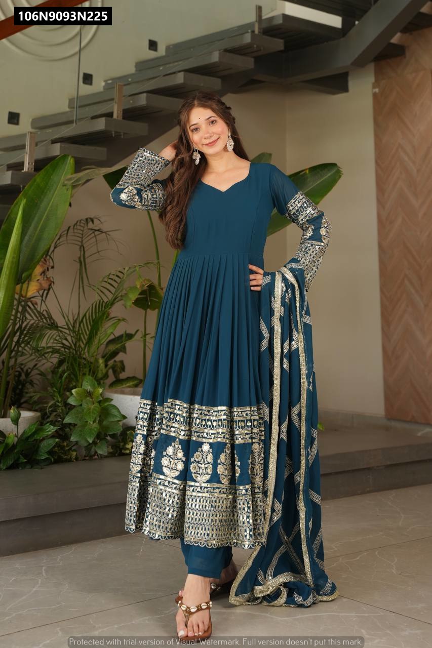 Model posing confidently in a TRENDBUY Teal Blue Fox Georgette Anarkali Gown Set, hand on hip, showcasing the detailed gold embroidery on the sleeves and border.