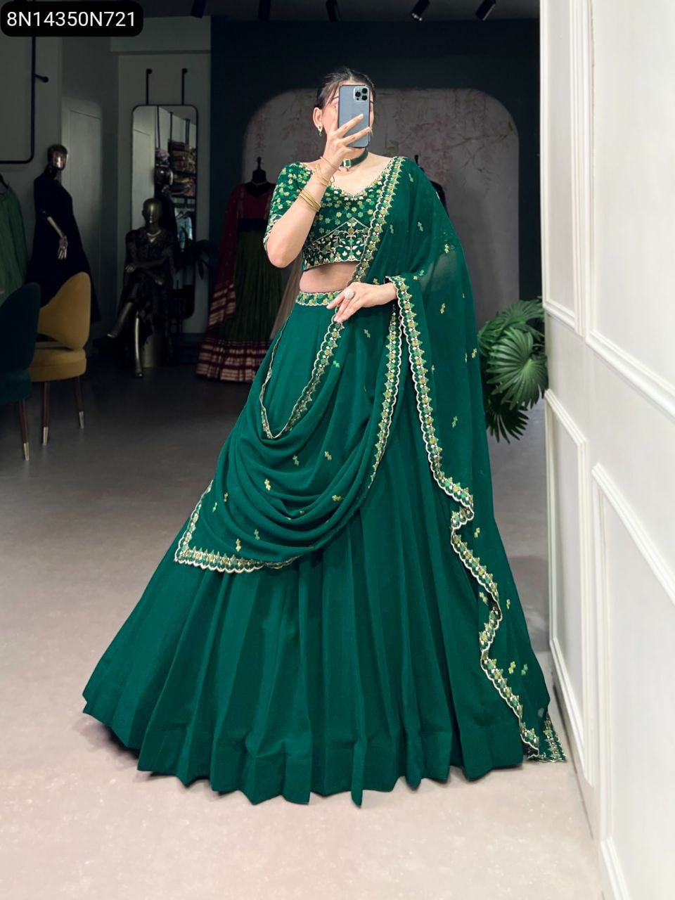 TRENDBUY model in full green embroidered georgette lehenga choli, front view, holding a phone in a vibrant indoor setting.