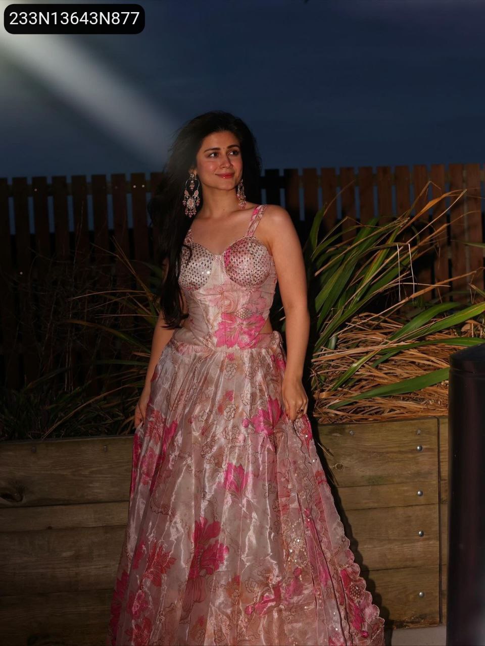 Full body shot of woman in TRENDBUY blush pink digital printed organza corset lehenga choli, standing outdoors against a fence.