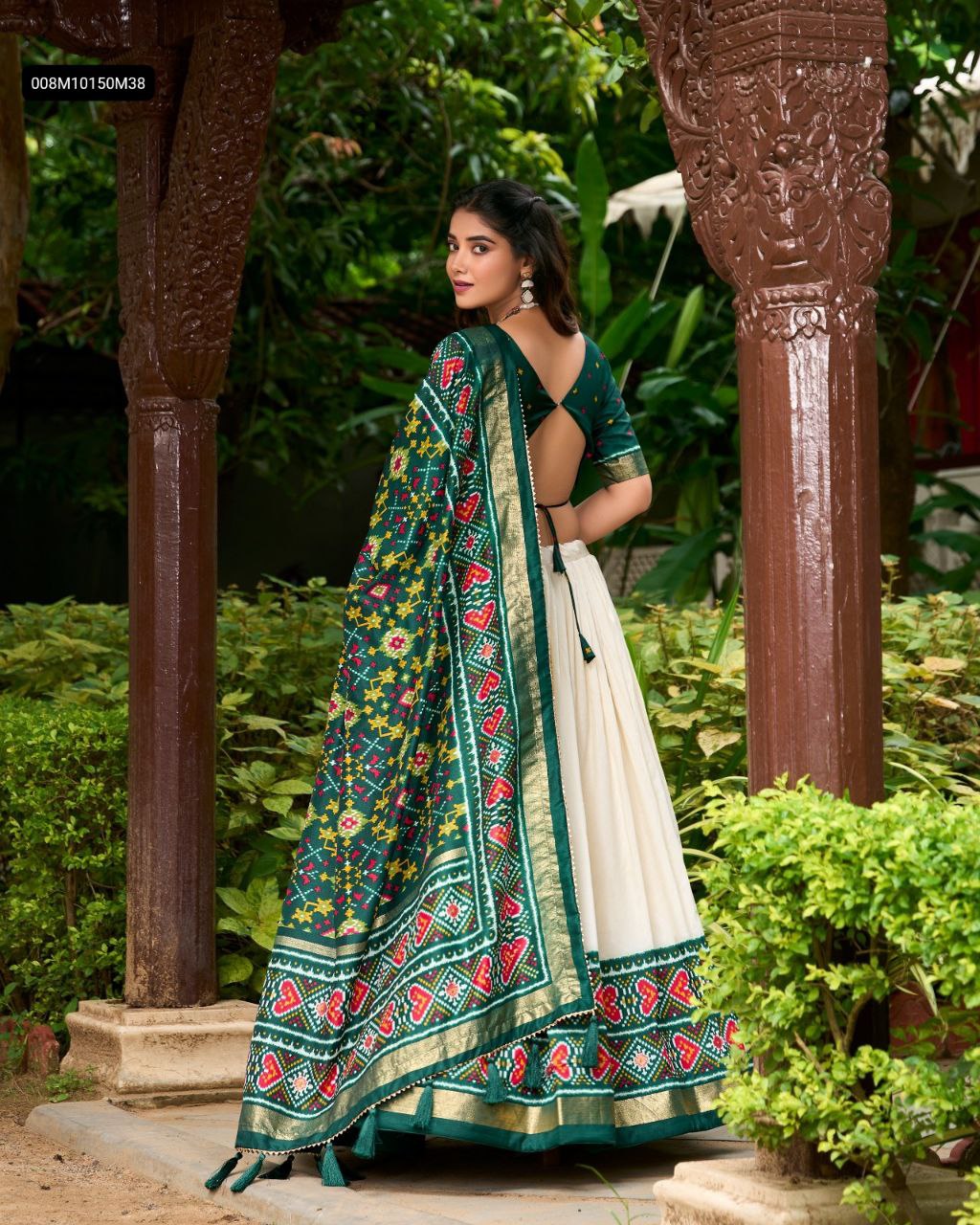 TRENDBUY Patola Print Tasar Silk Lehenga Choli with green blouse and dupatta, featuring intricate print and gold border, seen from the back in a garden setting.