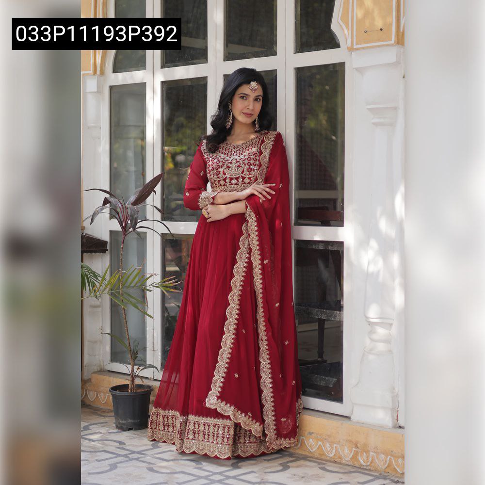 TRENDBUY model posing in a beautiful red embroidered Faux Blooming Anarkali gown with a matching dupatta, standing elegantly by a window.