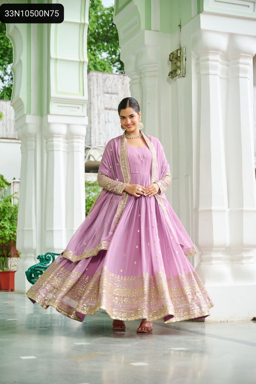 TRENDBUY Lavender Anarkali Gown with gold embroidery, full sleeves, and matching dupatta, worn by a model posing elegantly under an archway.