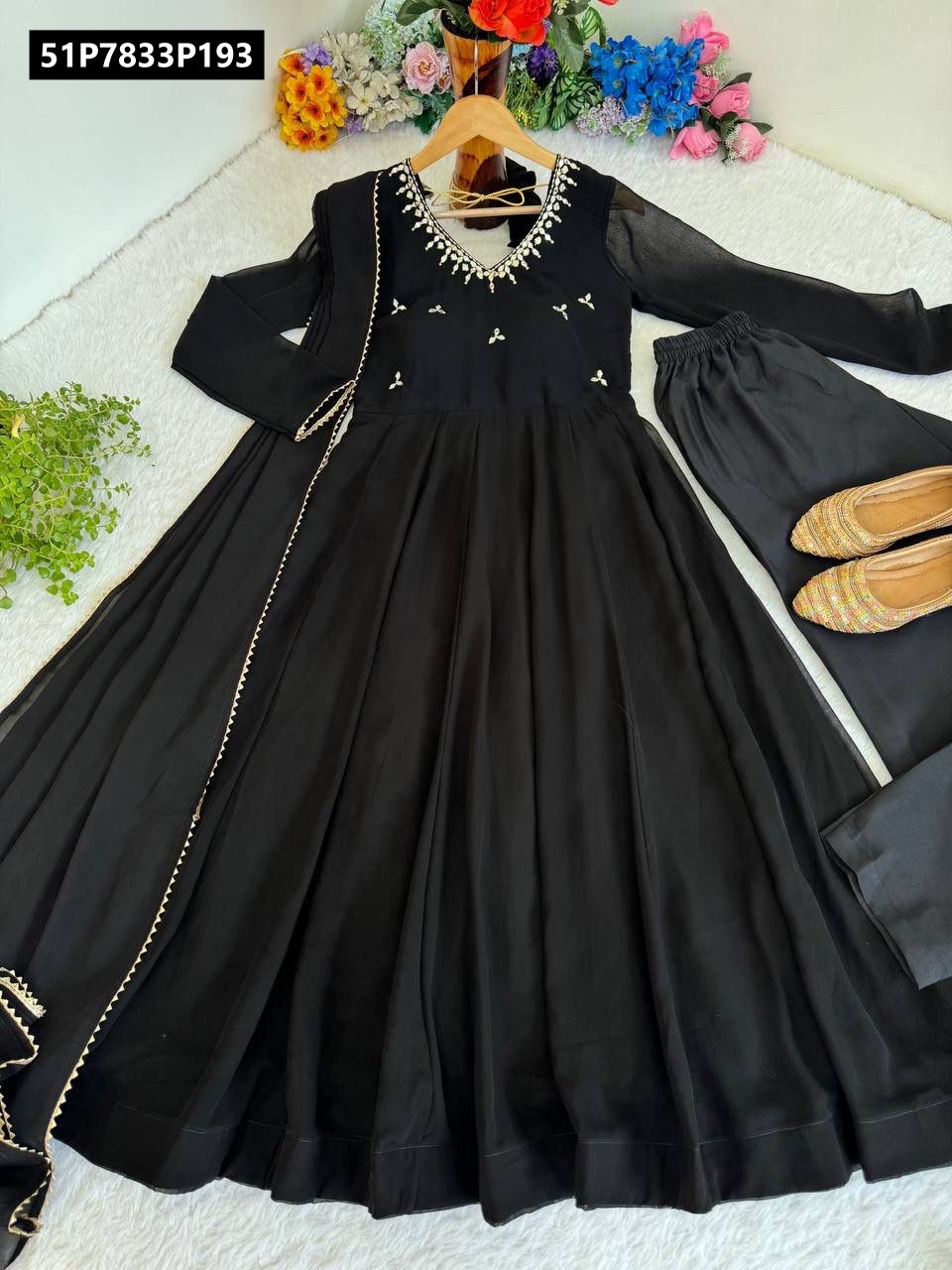 Full view of TRENDBUY black Fox Georgette Anarkali gown set with dupatta and bottom, displayed on a wooden hanger against a floral backdrop.