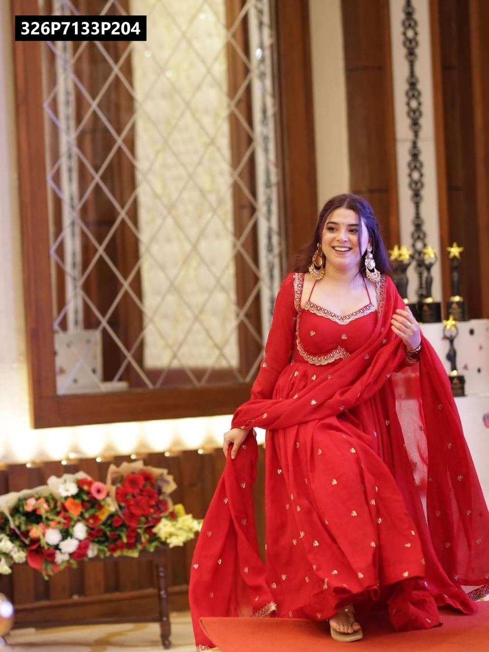 Dynamic full-body shot of the TRENDBUY model in a vibrant red embroidered Fox Georgette Anarkali suit set with dupatta, gracefully walking on a raised platform, capturing the outfit's elegant flow.